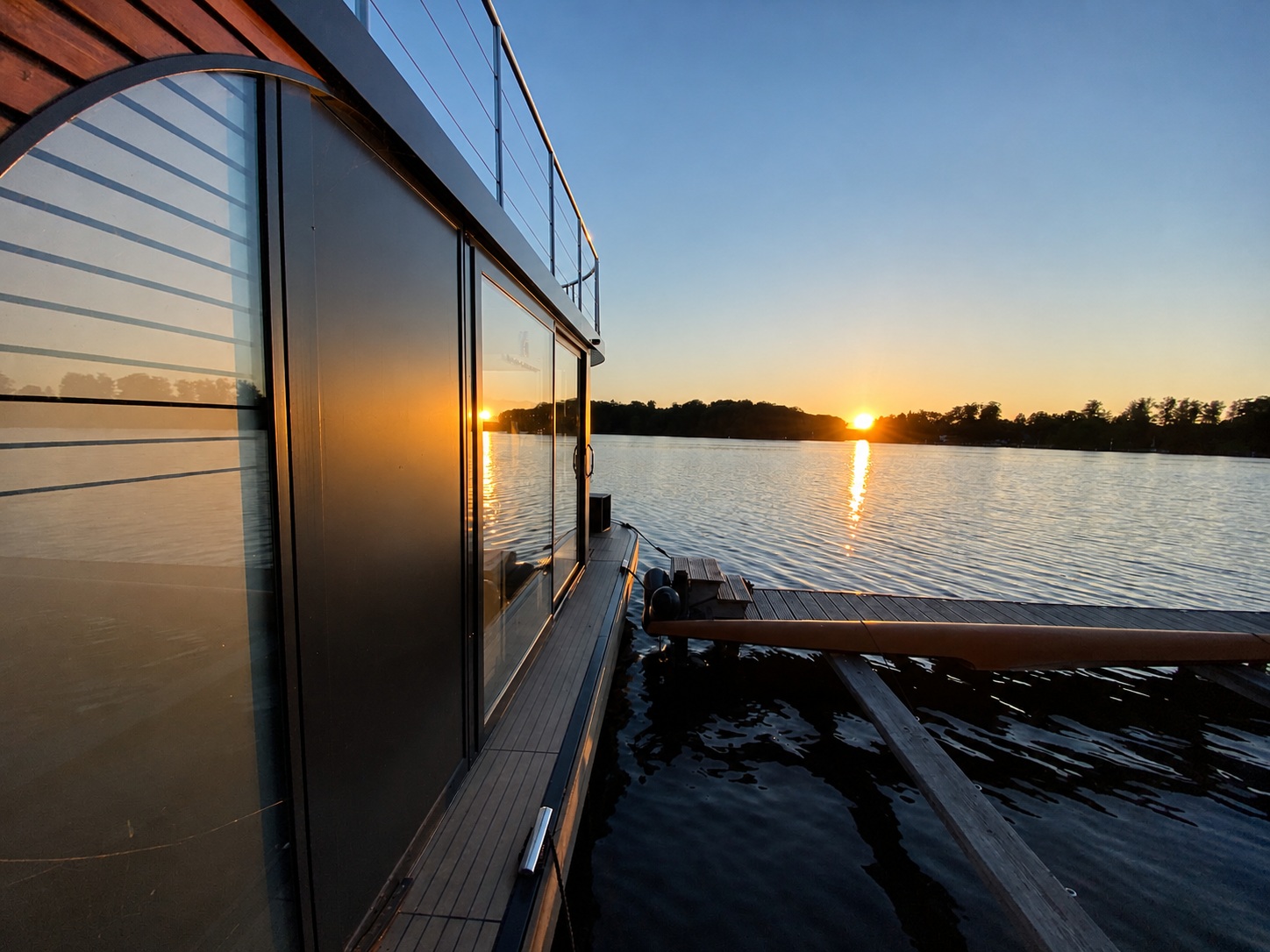 Blick an der Glasfront des Hausboots entlang über den Krüpelsee in den Sonnenuntergang