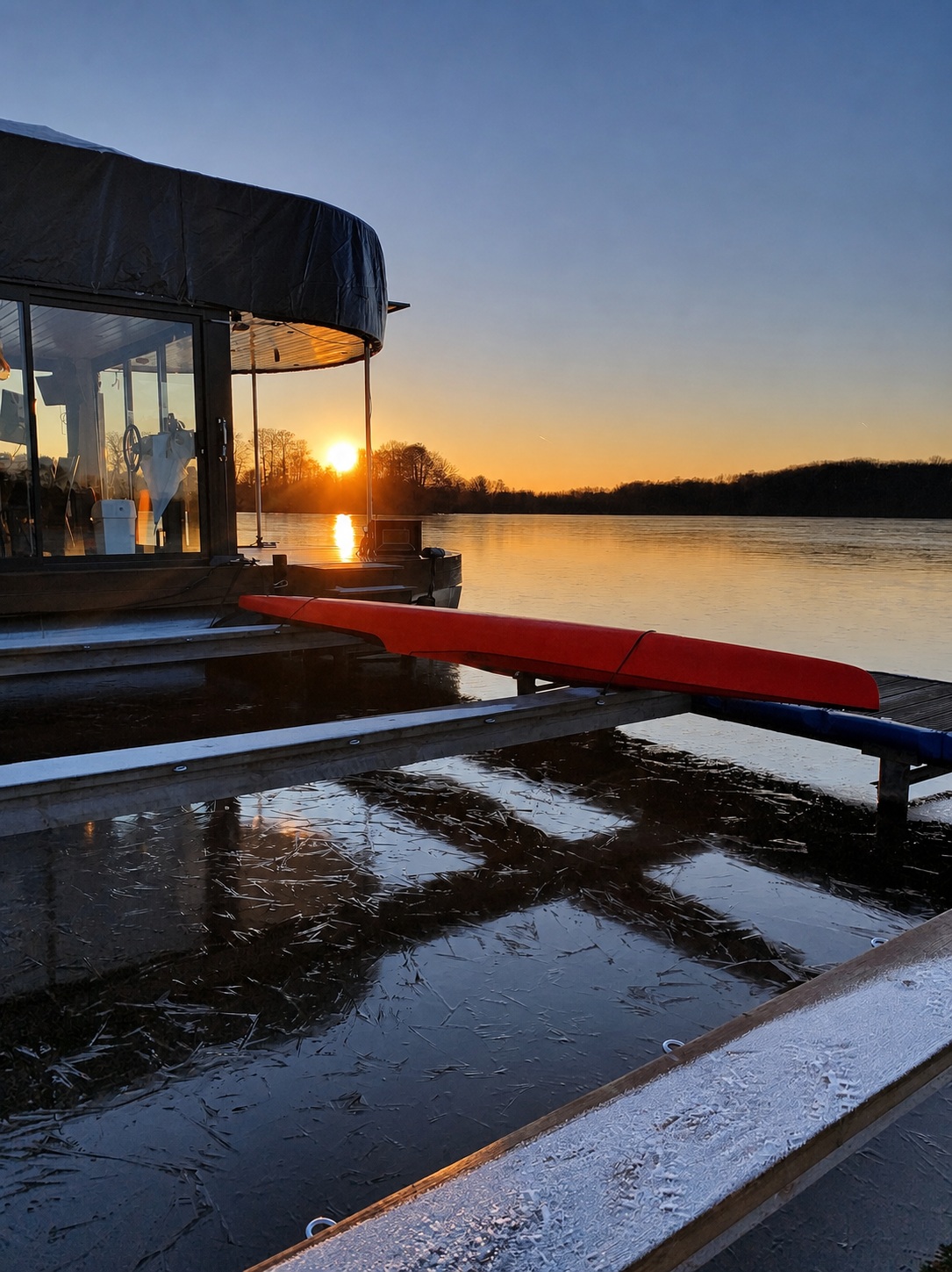 Das Hausboot mit Winterpersenning und Kajaks auf dem vereisten Steg bei tiefstehender Wintersonne