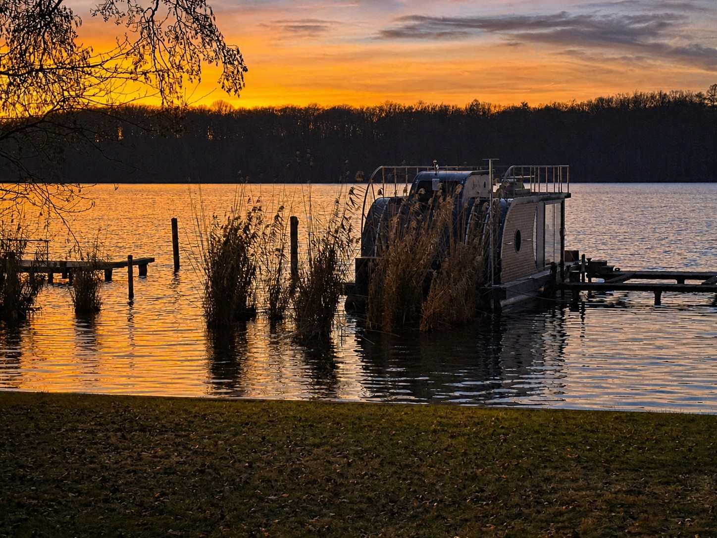 Das Hausboot Nautilus Maxi am eigenen Steg im Schilf des Krüpelsees vor einem orangefarbenen Sonnenuntergang
