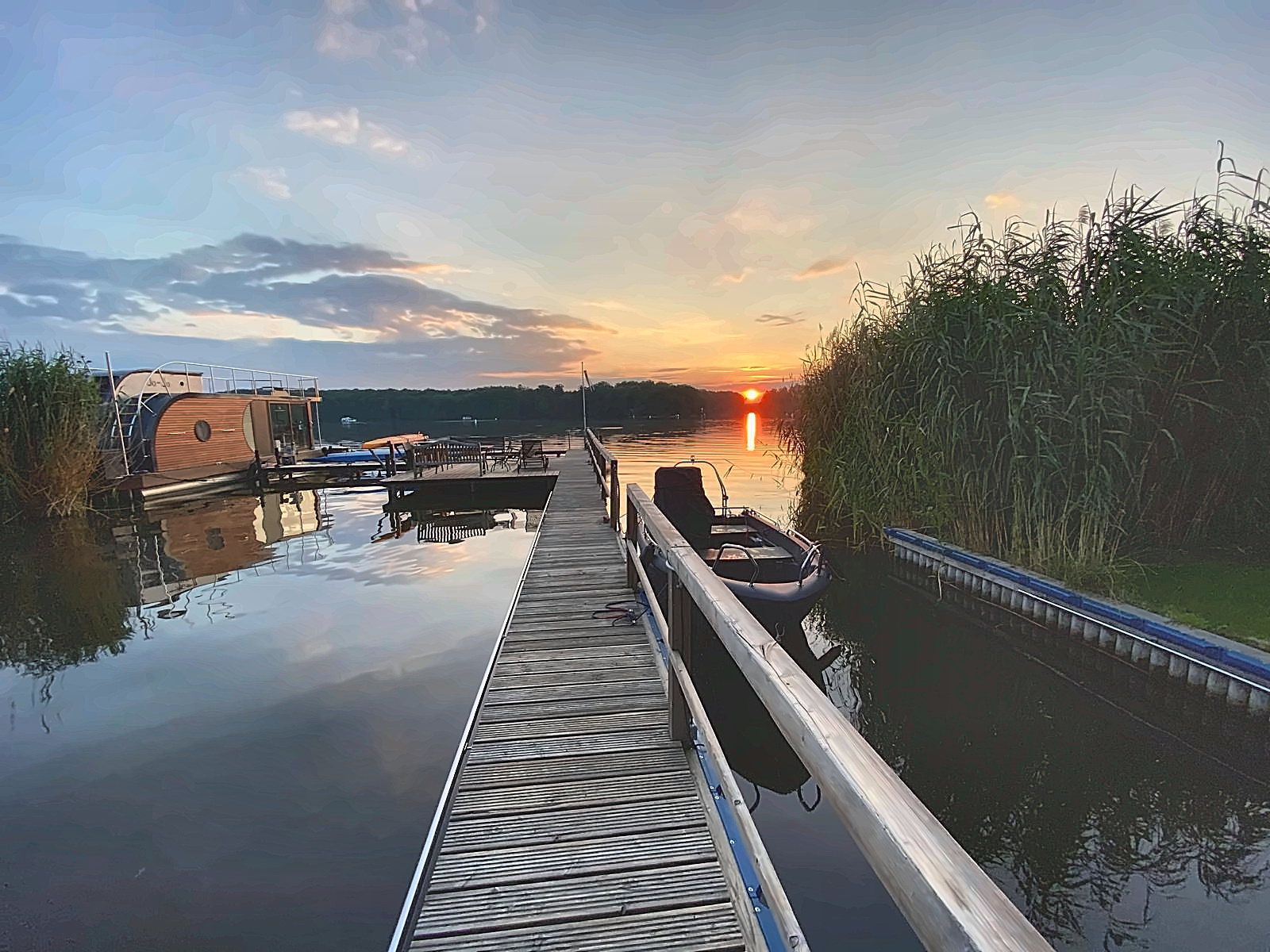 Blick entlang des eigenen Holzstegs am Krüpelsee mit festgemachtem Boot im Abendlicht
