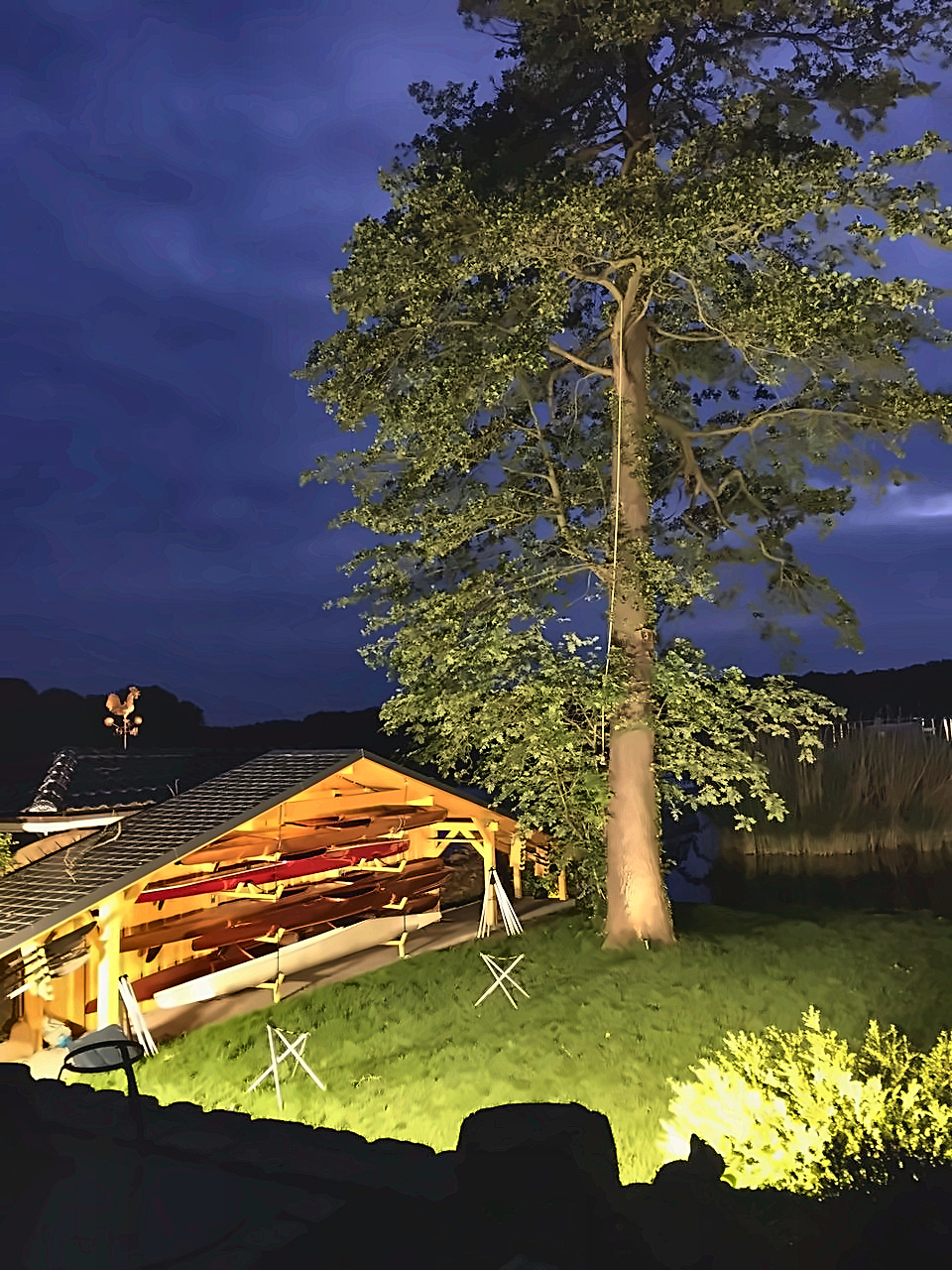 Beleuchteter Bootsunterstand mit eingelagerten Booten auf dem Seegrundstück bei Nacht